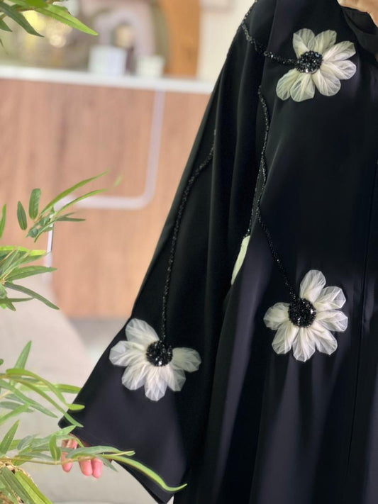 Black Abaya with white floral embroidery on a blurred indoor background